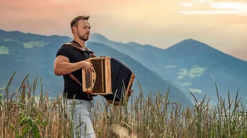 Mann spielt Steirische Harmonika in einer Berglandschaft